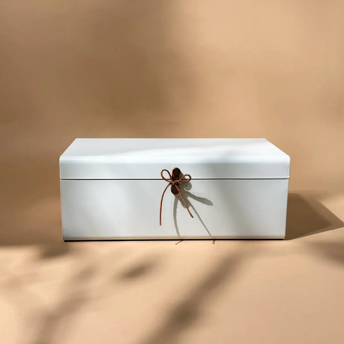 Matte white steel storage trunk with tan leather tie, centred on tabletop