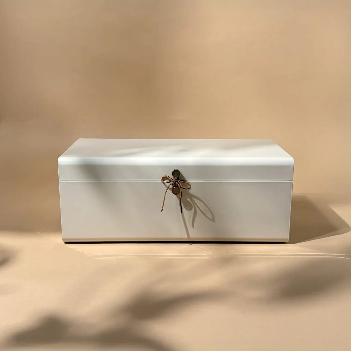 Matte white steel trunk box with leather tie closure, centred straight-on shot