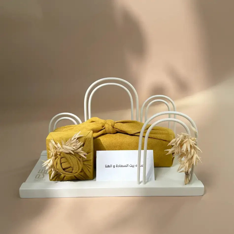 Mustard fabric-wrapped gifts on white arch stand with dried wheat and New Home card