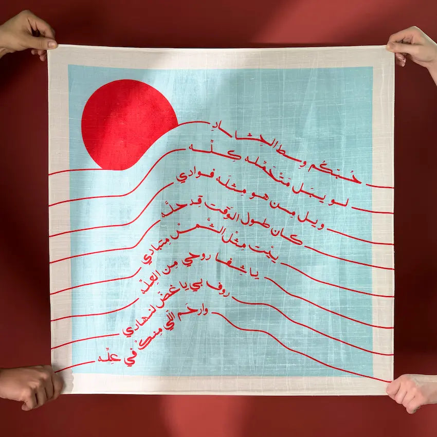 Printed fabric gift wrap held open, red sun and Arabic script on light blue