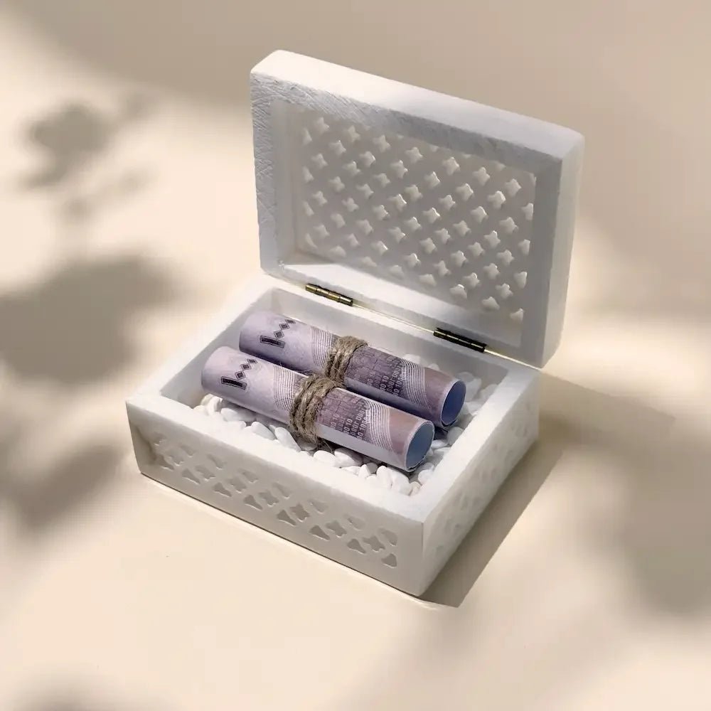 Open marble cutout box showing rolled cash tied with twine on white pebbles