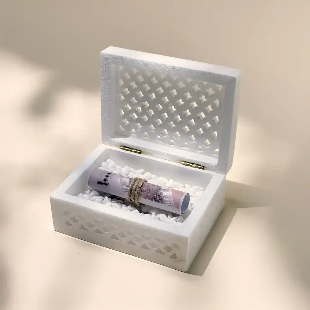 Open white carved marble box holding rolled cash on pebbles, twine detail visible