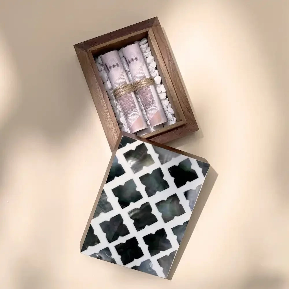 Open rosewood cash box showing folded notes on white pebbles, lid with pearl tile pattern