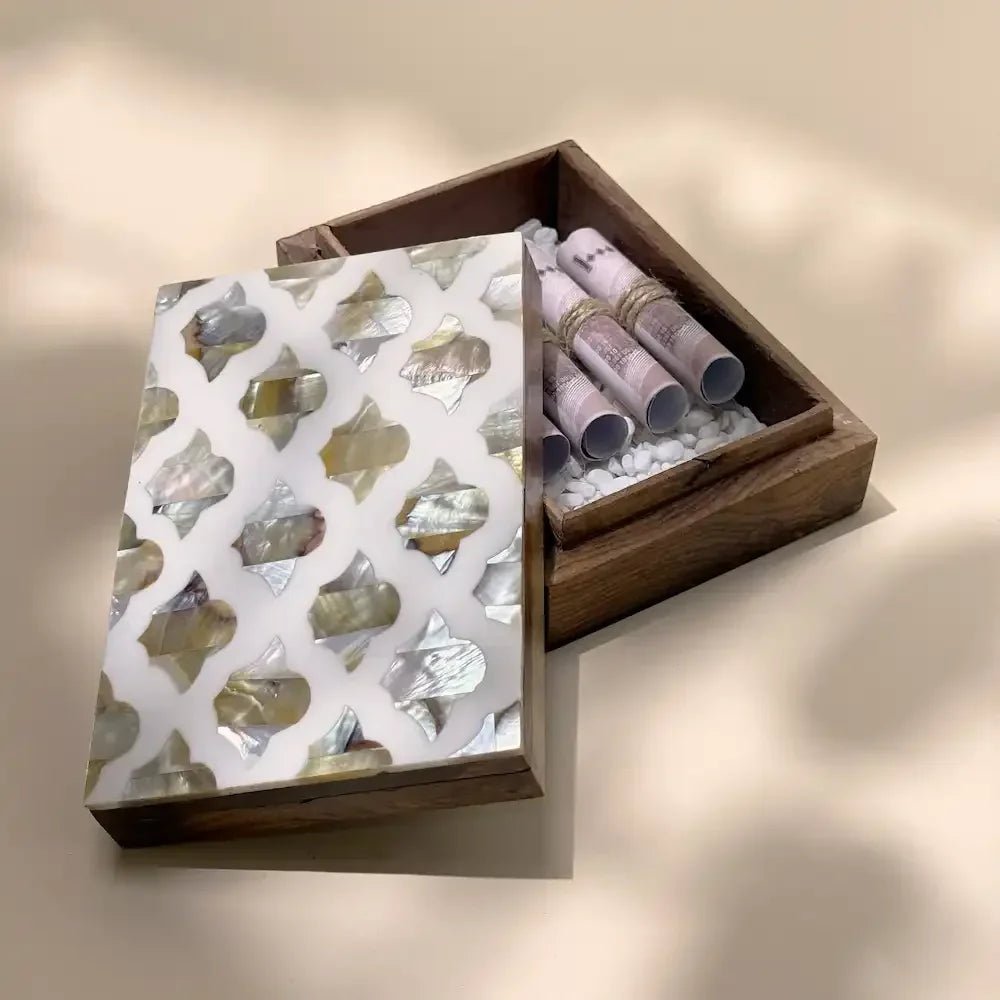 Open mother-of-pearl inlay wooden box showing rolled cash on white pebbles