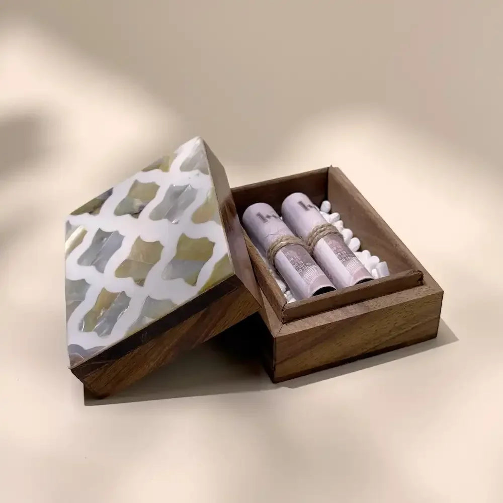 Mother of pearl lid beside open rosewood box with cash rolls on pebbles