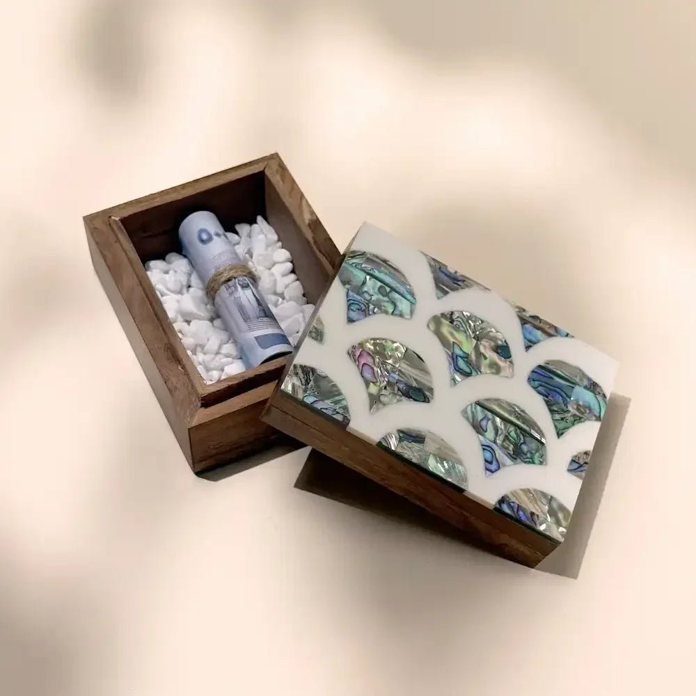 Open mother of pearl inlay wooden box showing rolled cash on white pebbles beside closed lid