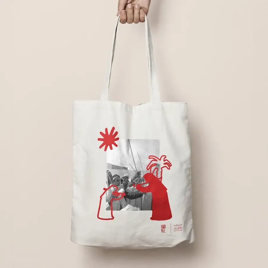 Hand holding cream tote bag with red Al Ayyala illustration and palm tree print