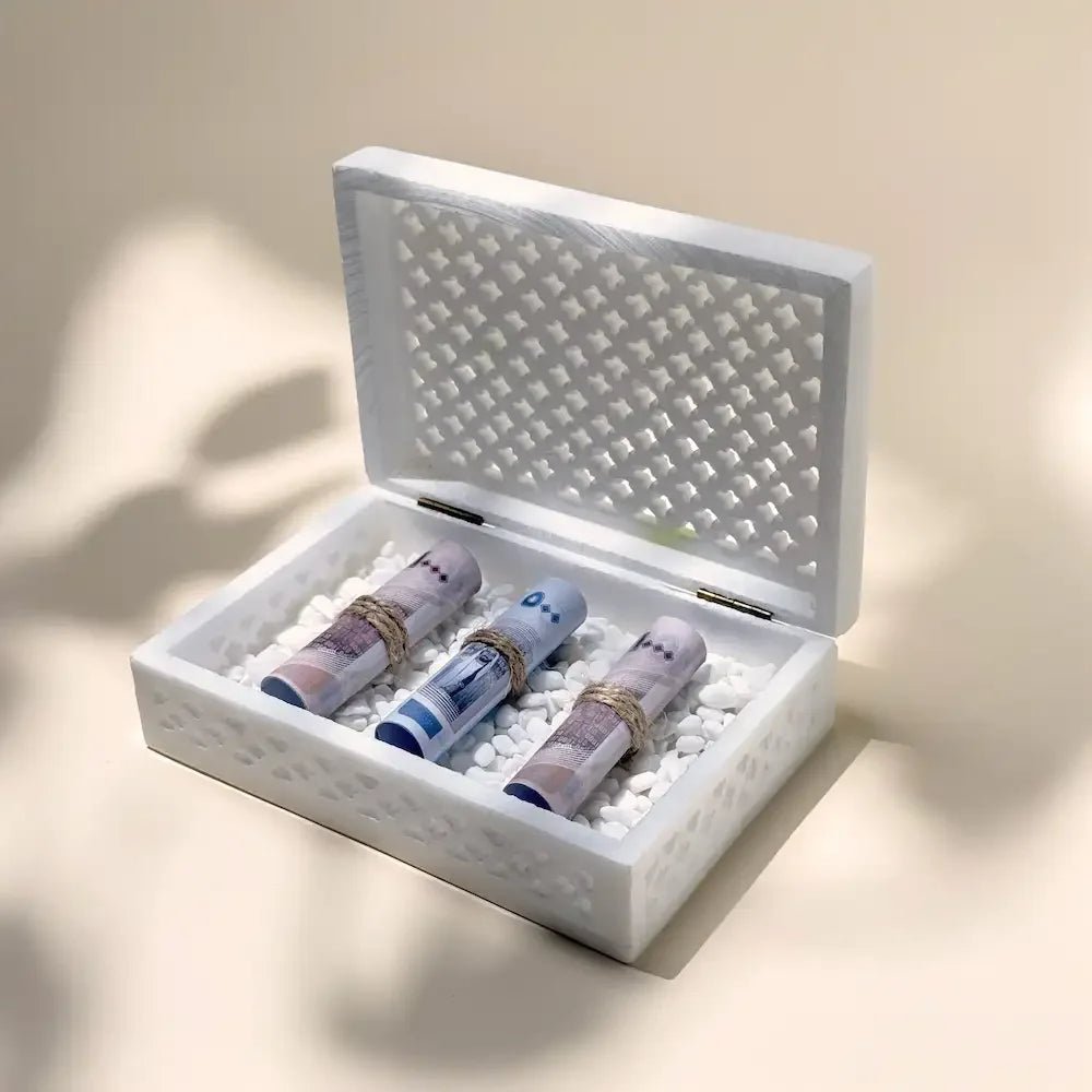 Open white marble cutout money box with cash rolls nestled on white pebbles