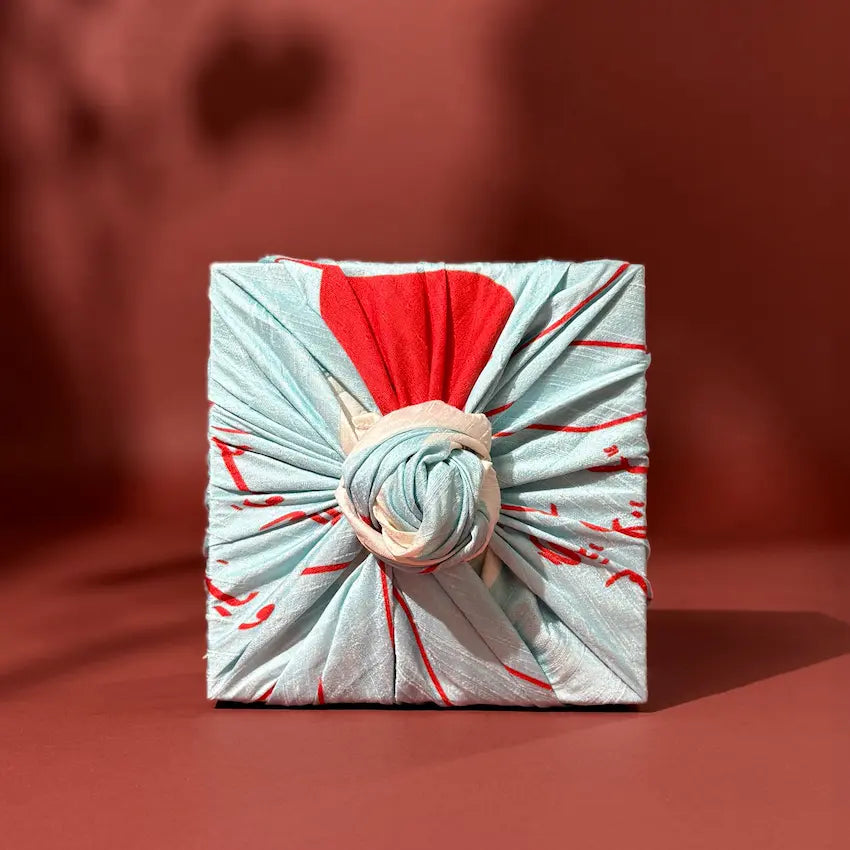 Gift box wrapped furoshiki-style in red and pale blue patterned cloth, knot detail