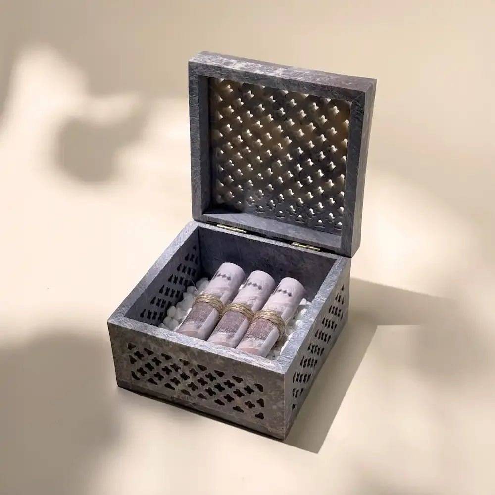 Open grey marble-style money box with cash rolls nestled in white pebbles