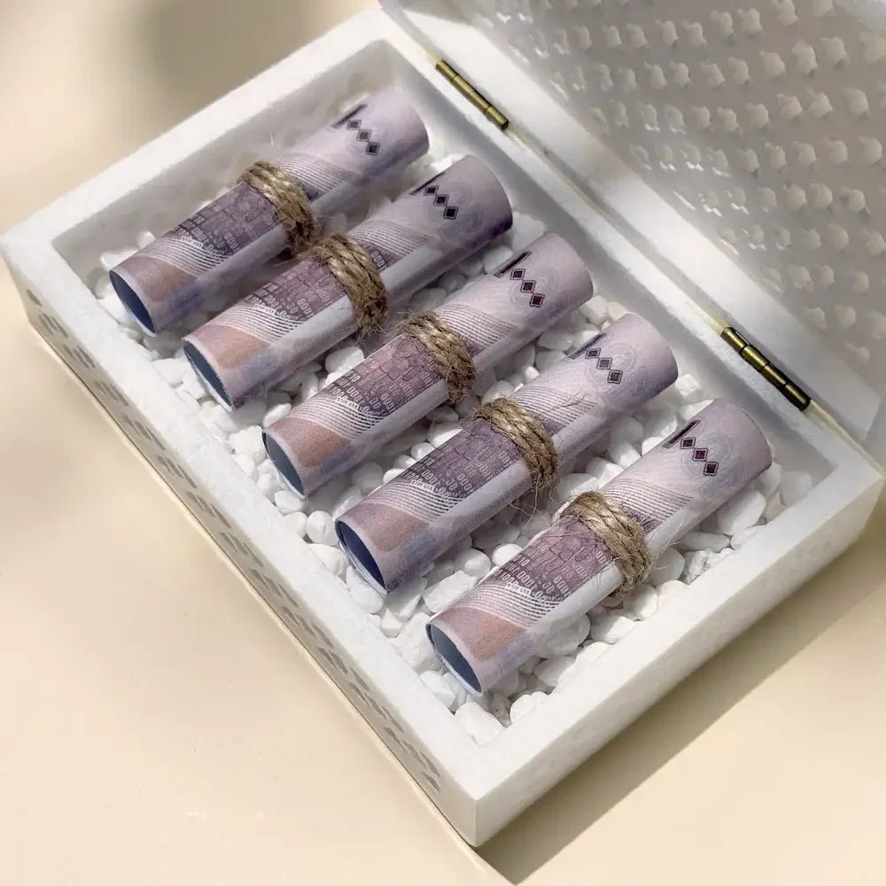 Close-up of rolled banknotes tied with twine, nestled in white pebbles inside marble box