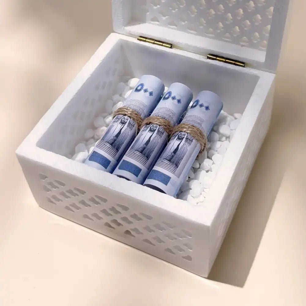 Close-up of cash rolls nestled in white stones inside marble gift box