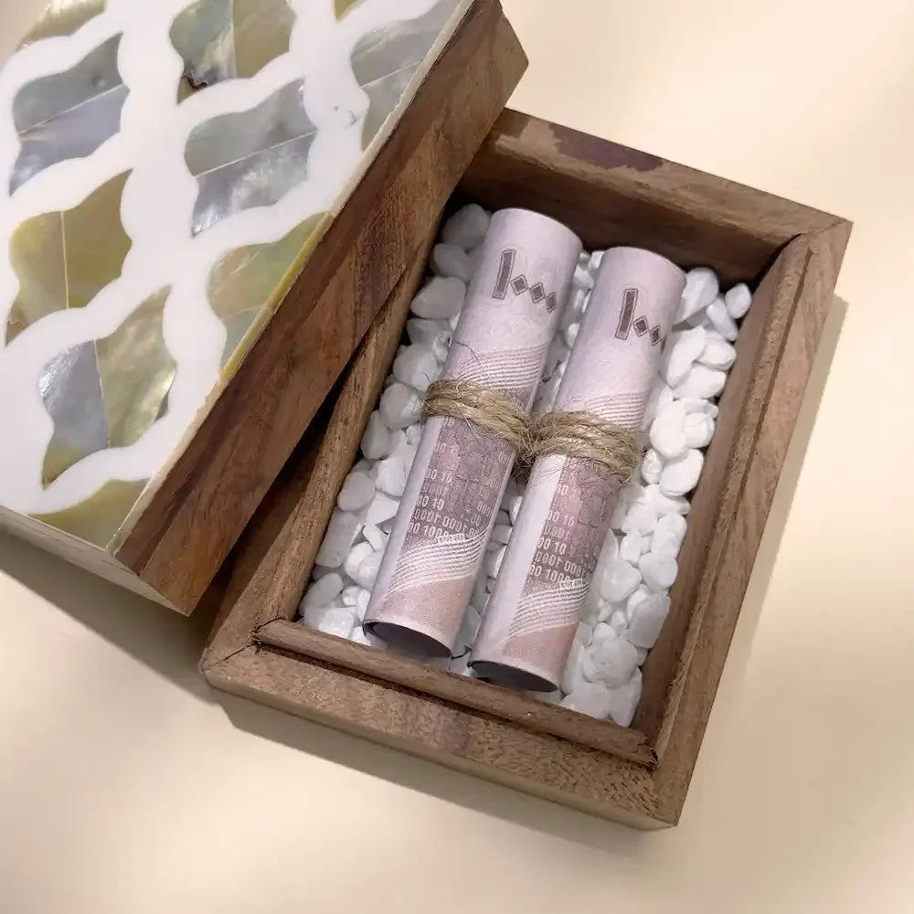 Close-up top view of cash rolls nestled in white pebbles inside wooden box