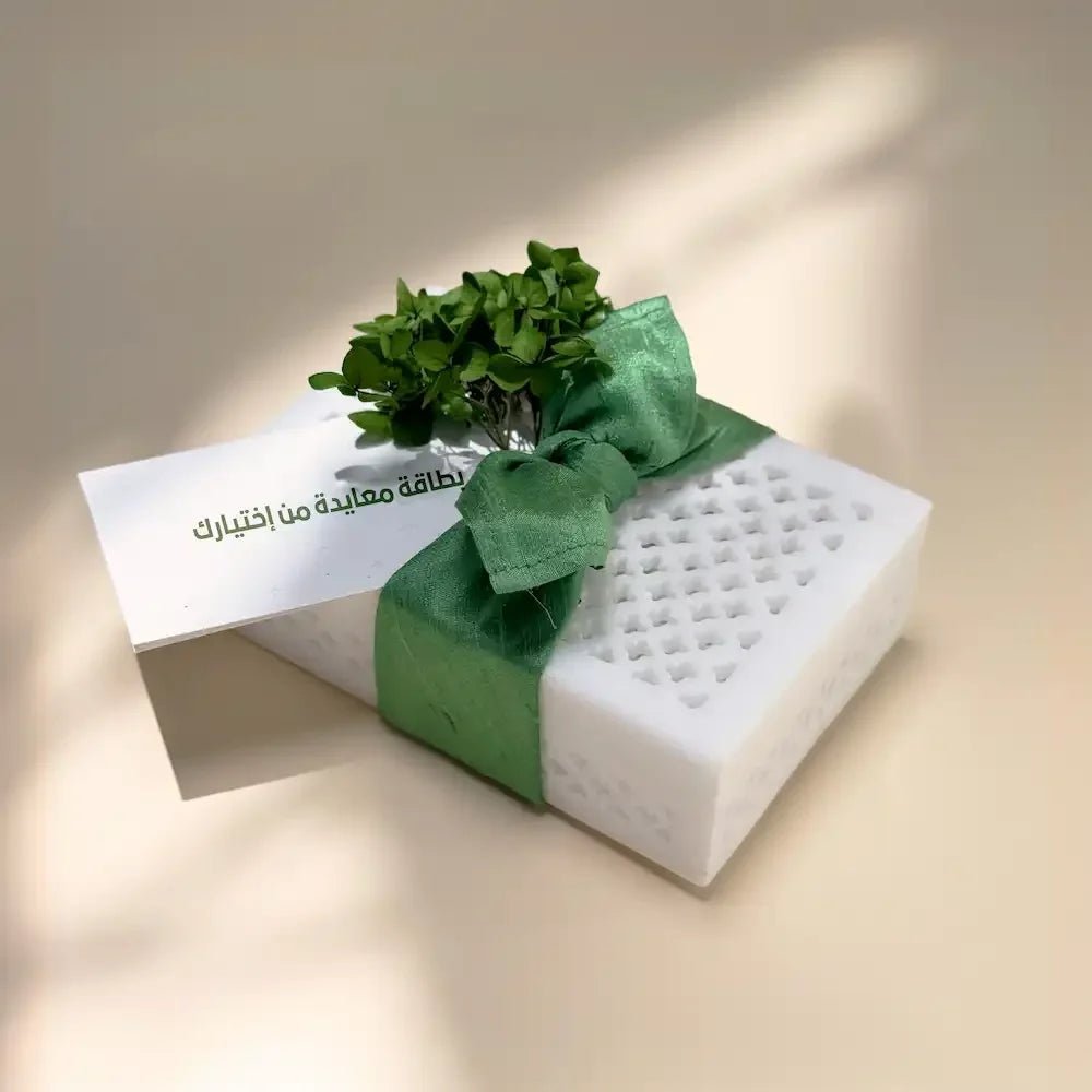 White marble-style cash box tied with sage green bow and greenery, greeting card beside it