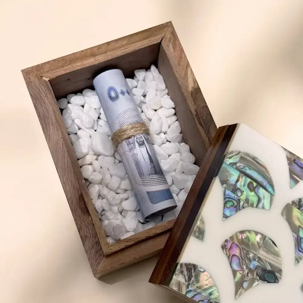 Close-up of rolled banknote nestled in white stones inside open rosewood keepsake box
