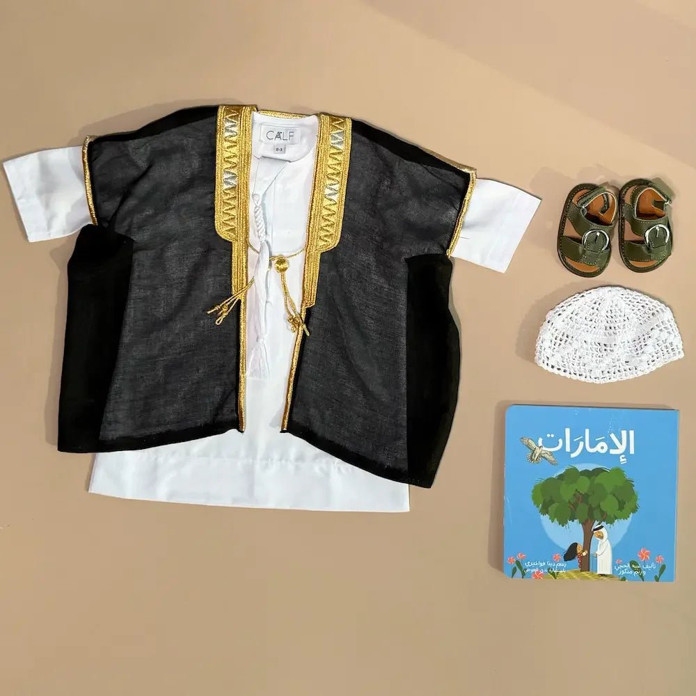 Flat lay of black and gold bisht, white kandura, kufi cap, sandals and UAE storybook