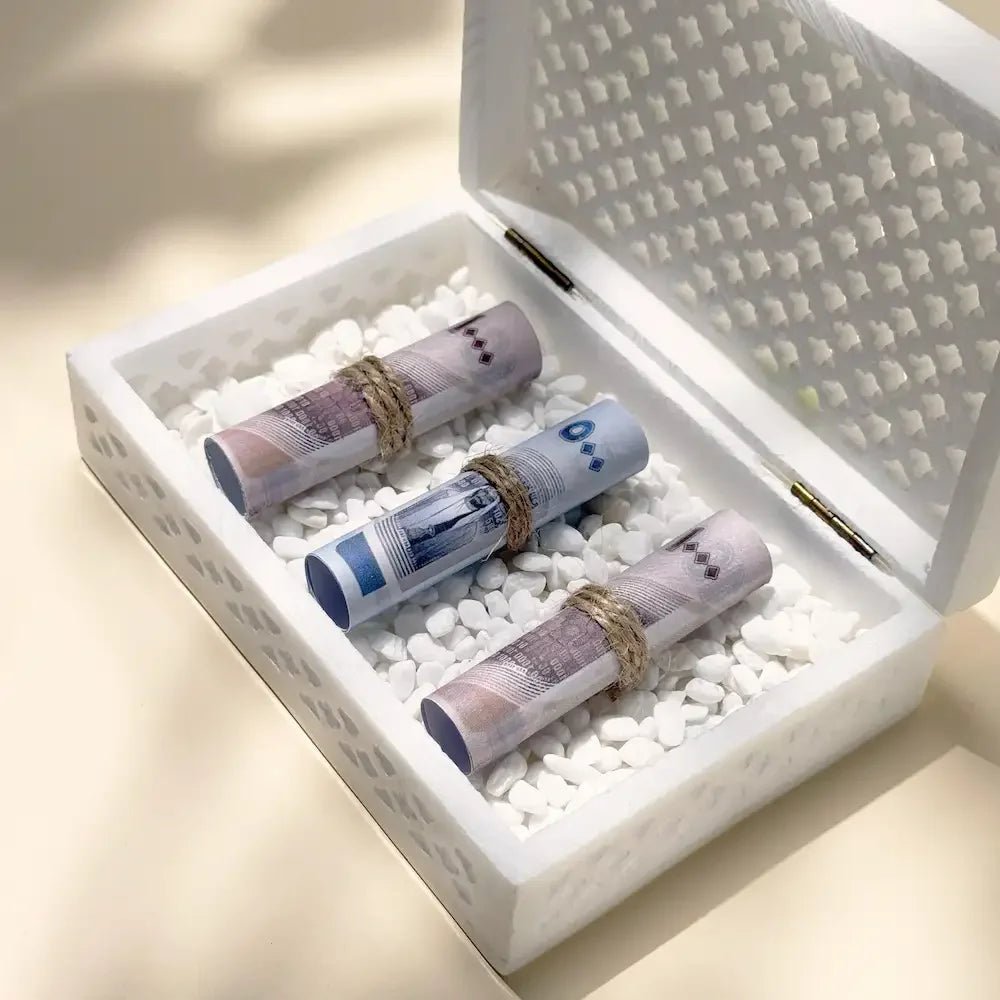 Close-up angle of cash rolls tied with twine inside white stone gift box