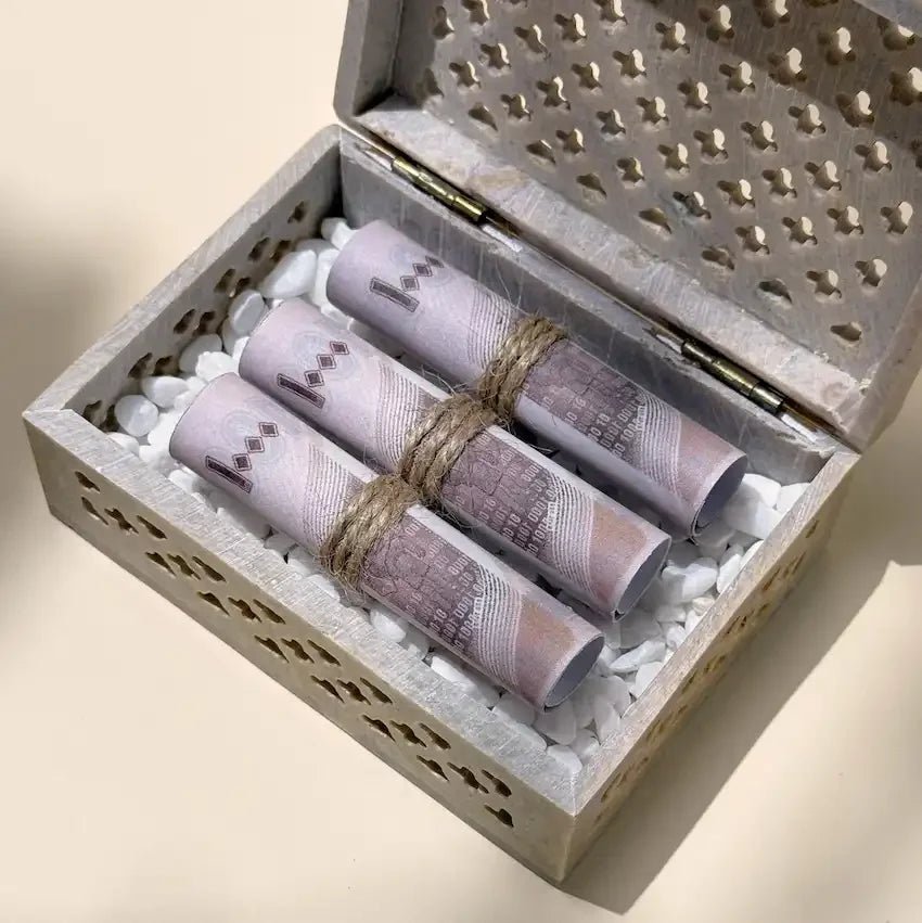 Close-up of cash rolls nestled in white pebbles inside carved stone box
