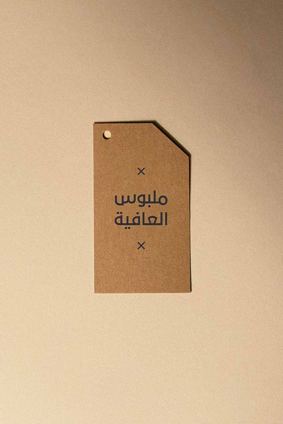 Kraft tag garment gifts card with Arabic script, hole punch, on beige background