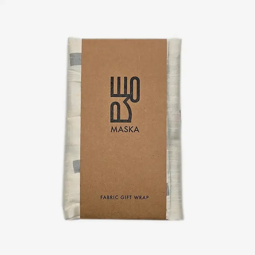 Folded printed fabric gift wrap with kraft Maska sleeve label, silver dot pattern edges visible