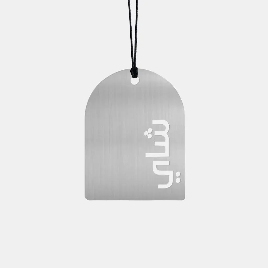 Silver metal trinket with cutout Arabic word 'shai', hanging on black cord