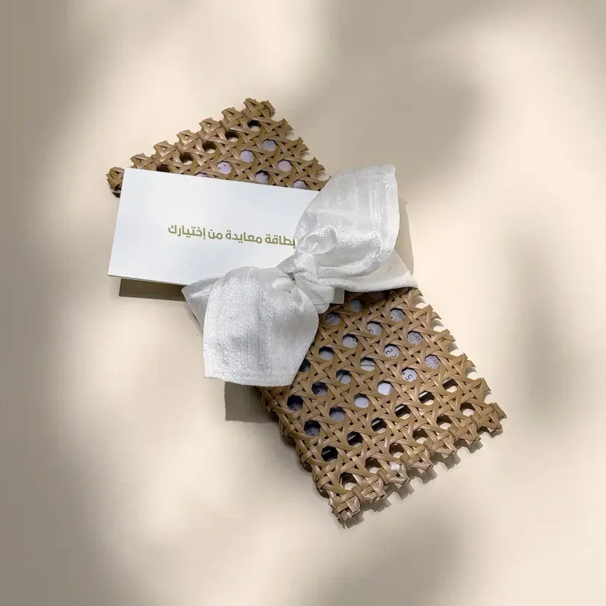 Rattan cash pouch with off white bow and blank greeting card on beige backdrop