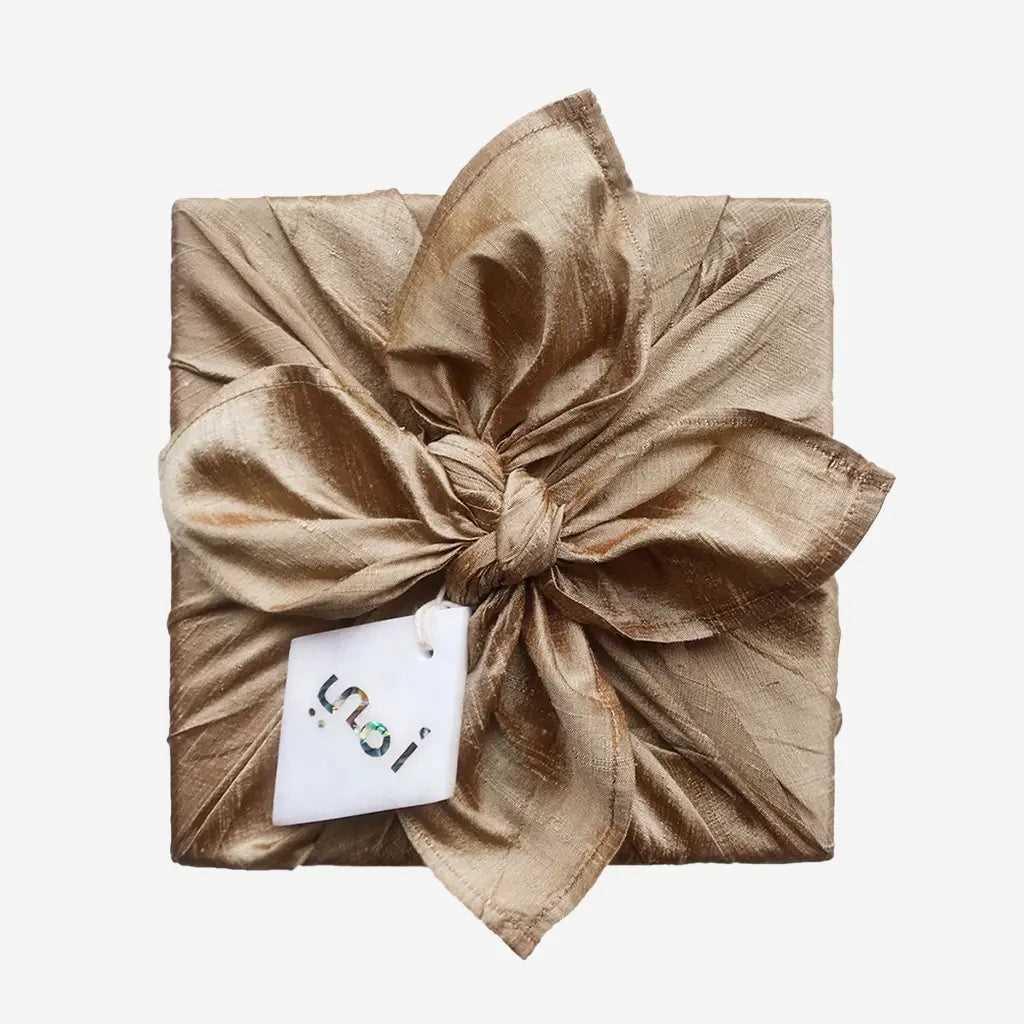 Marble charm tied to a gold silk furoshiki-wrapped gift box