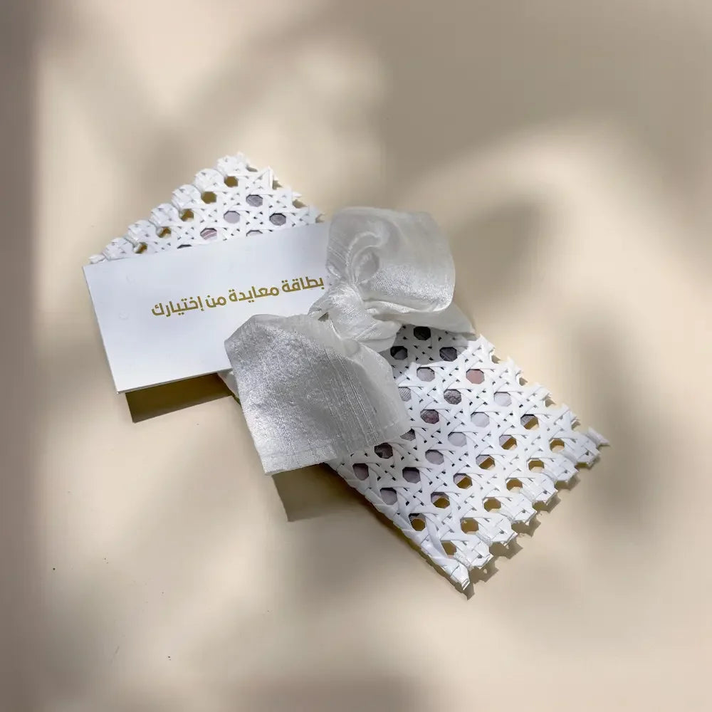 White rattan cash pouch tied with off white fabric bow beside matching greeting card