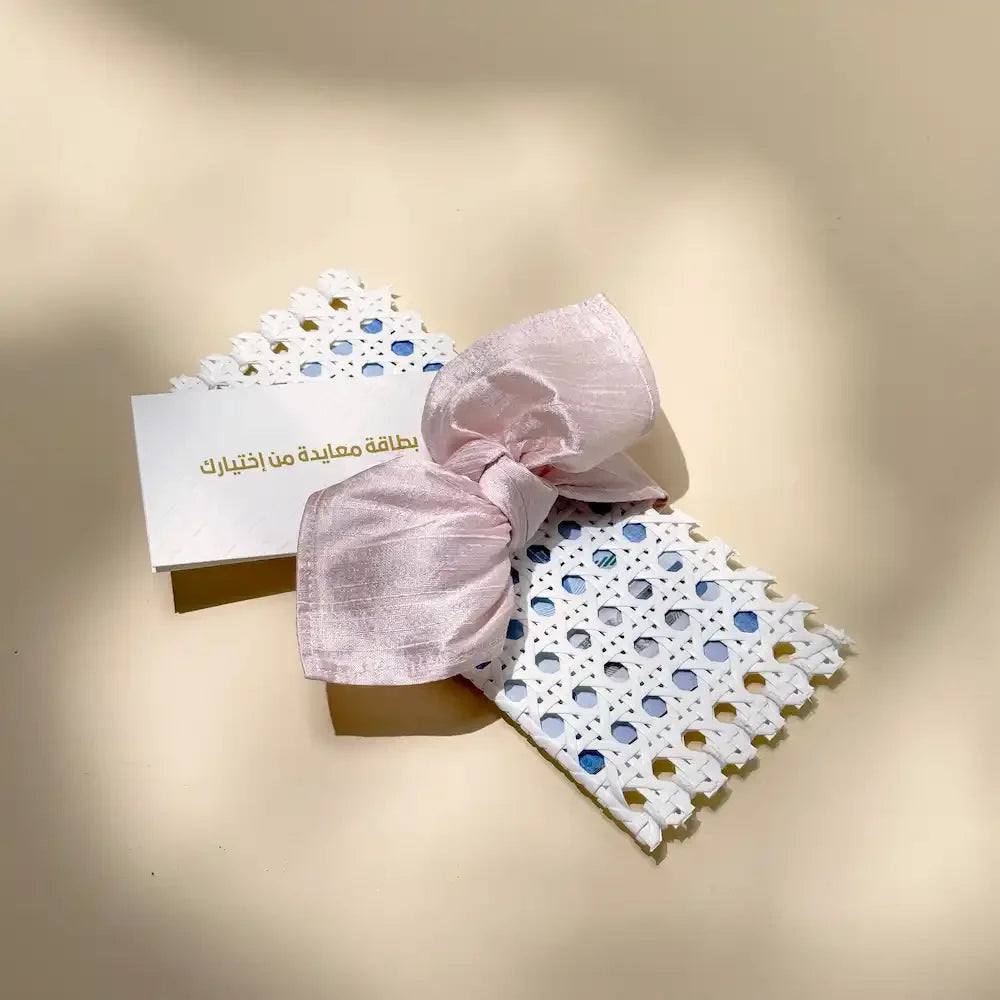 White rattan cash pouch with pastel pink fabric bow beside a matching greeting card