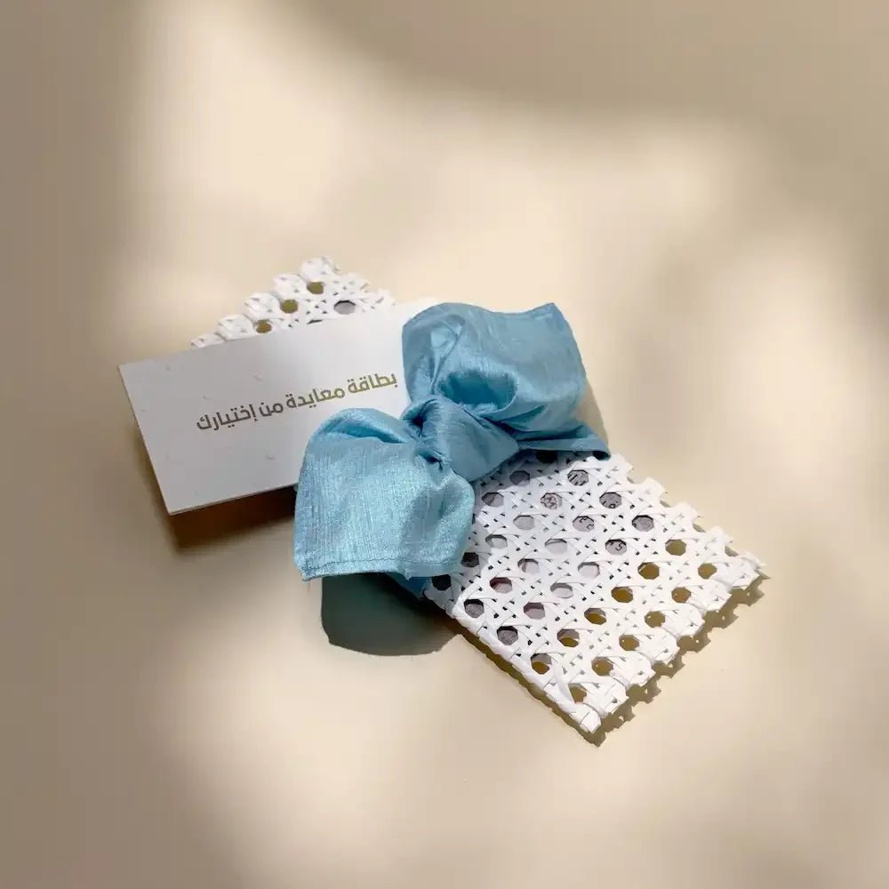 White rattan cash pouch tied with baby blue fabric wrap beside a greeting card