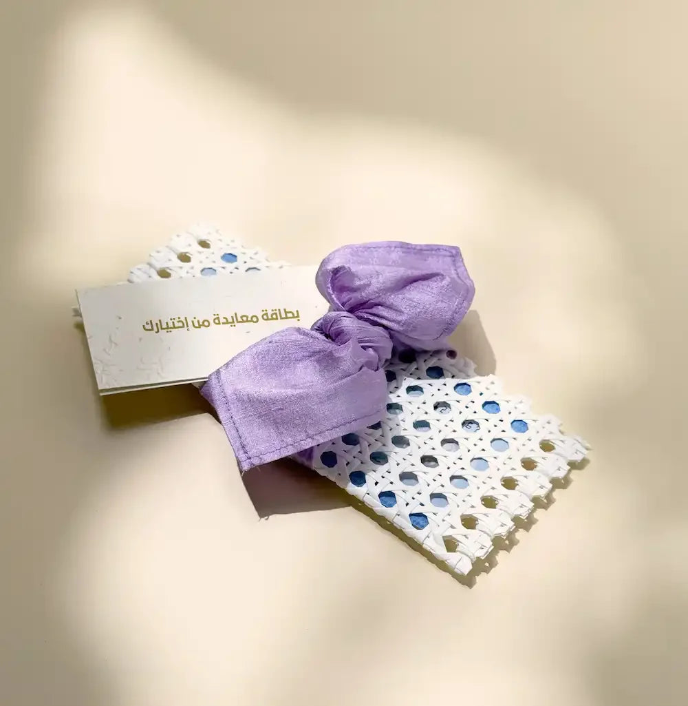 White rattan cash pouch tied with lavender fabric wrap beside a greeting card