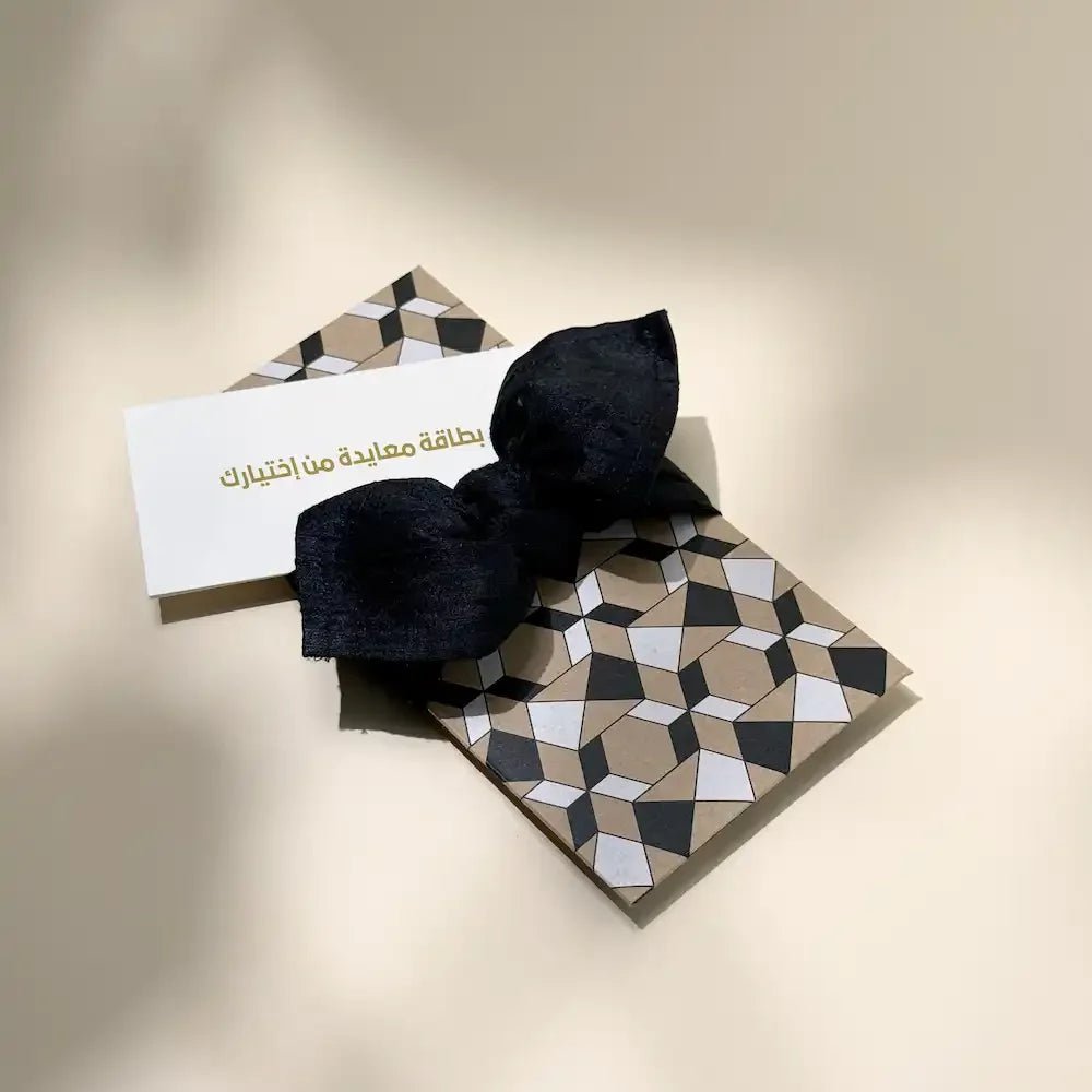 Geometric cash envelope with black fabric bow beside a blank greeting card