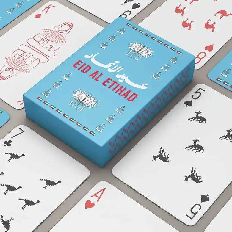 Teal Eid Al Etihad card box resting atop scattered camel and deer motif cards