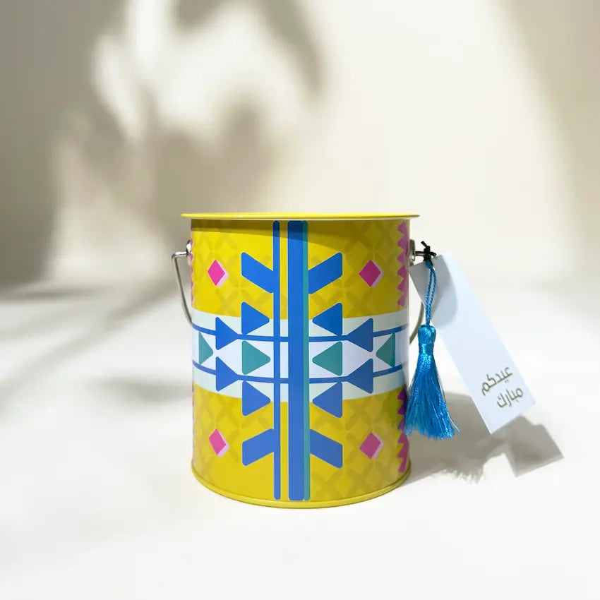 Yellow Sadu-patterned metal can with wire handle and blue tassel tag