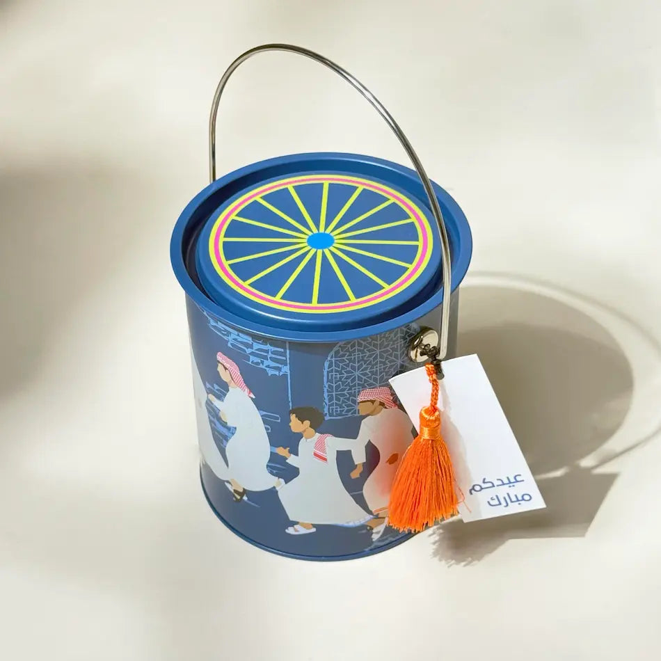 Overhead view of navy tin can with colourful wheel lid design and wire handle