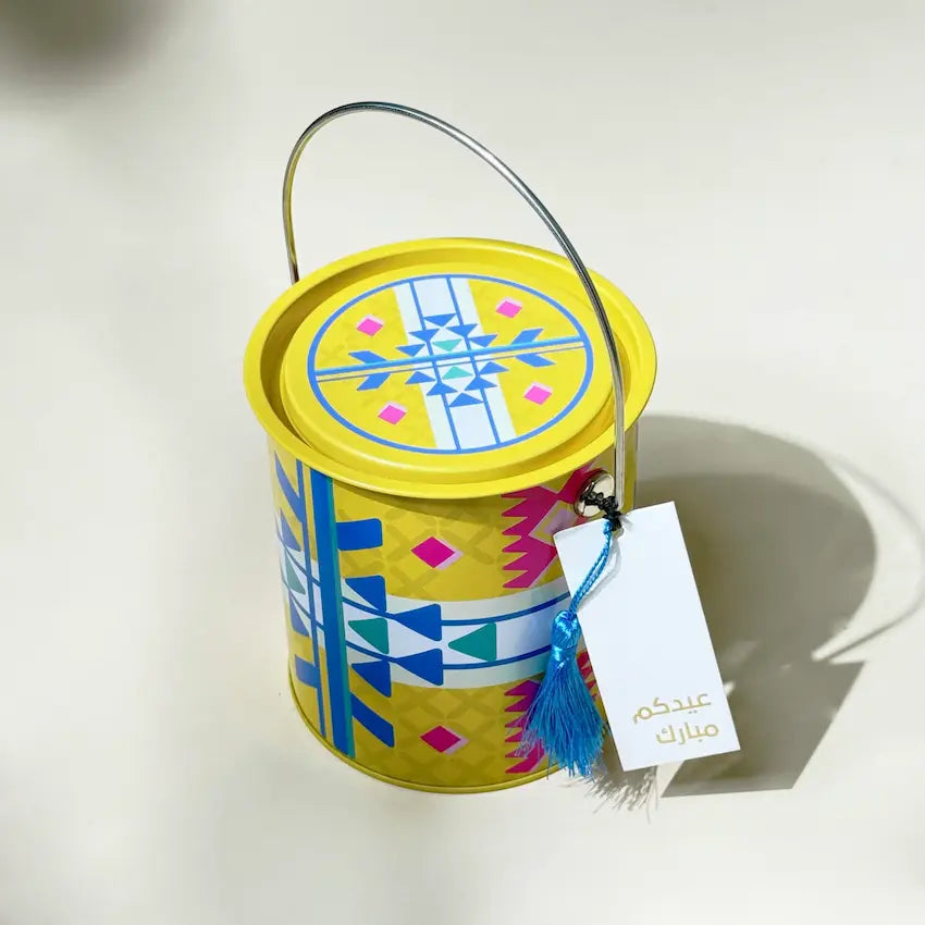 Top-down angle of yellow Sadu tin can with lid and Eid greeting tag