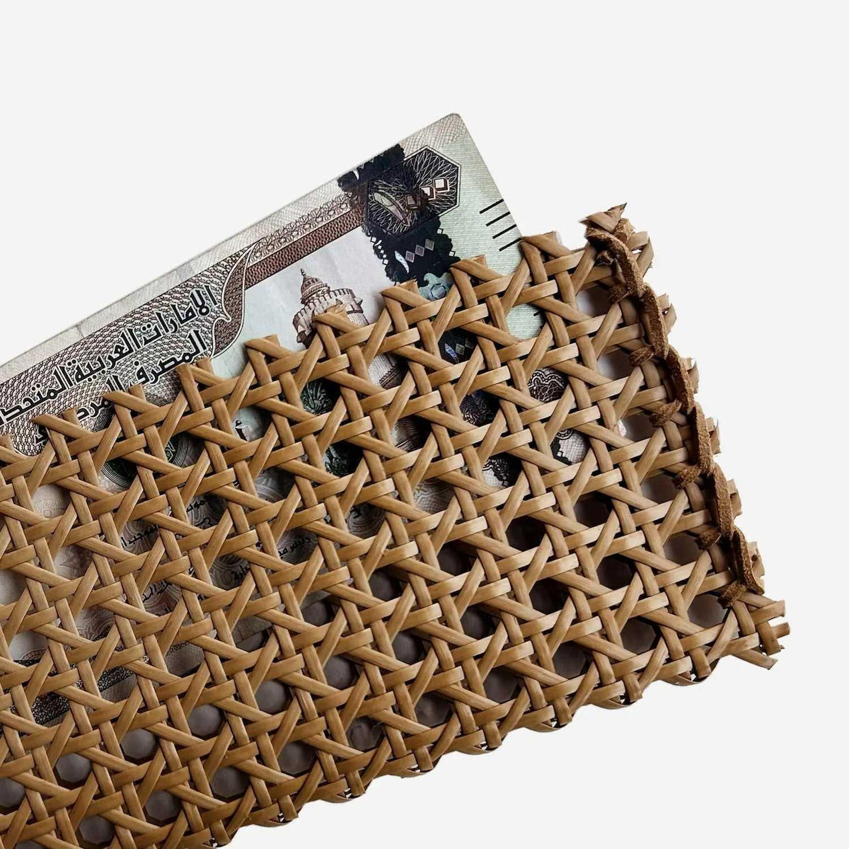 Close-up of woven rattan cash pouch corner holding UAE banknote