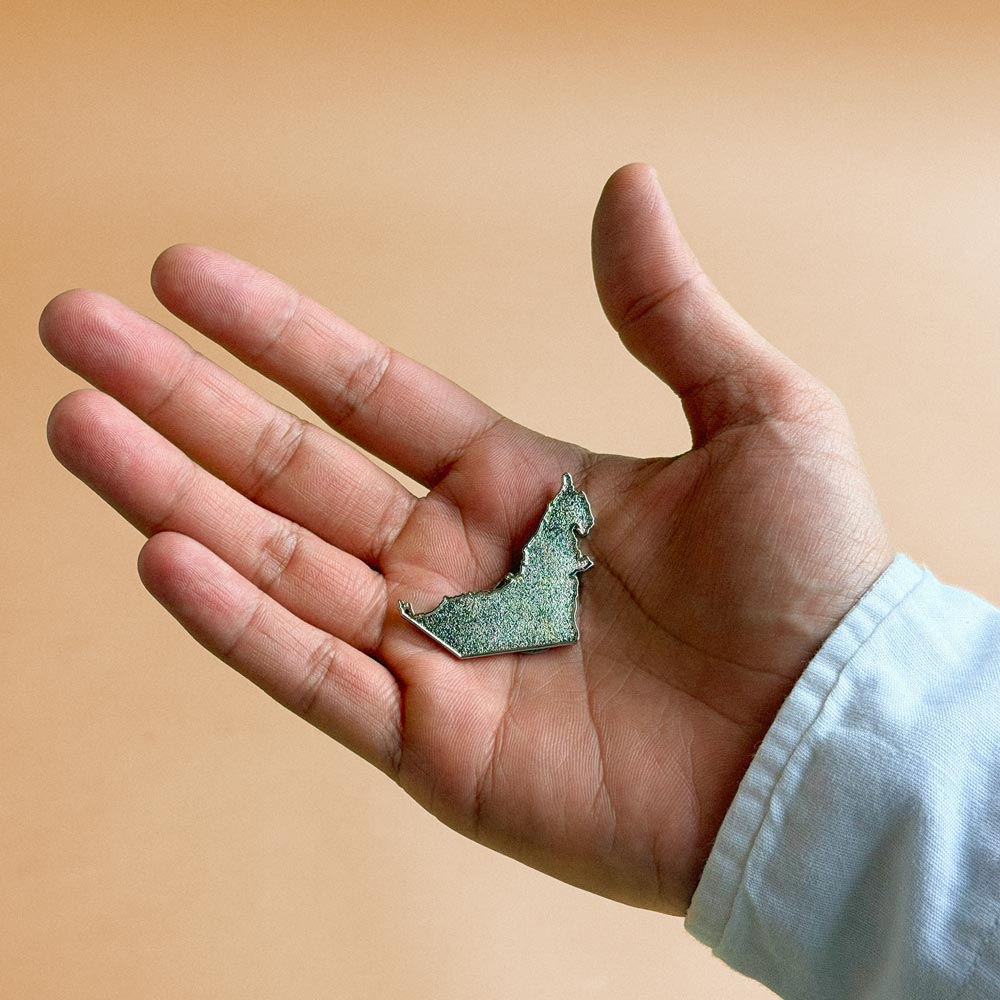 Silver UAE map pin held in the palm of a hand