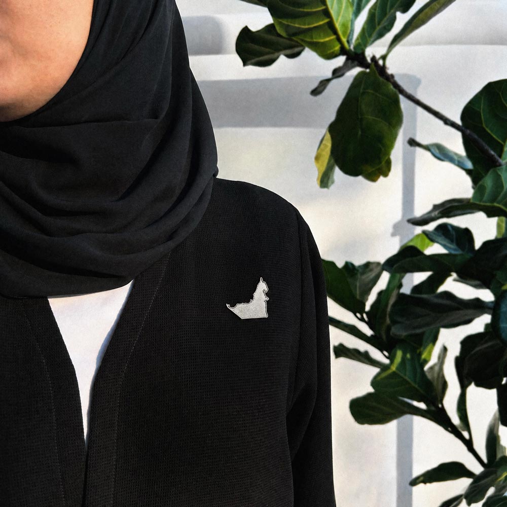 Silver UAE map pin worn on a black abaya